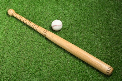 Photo of Wooden baseball bat and ball on green grass, above view. Sports equipment