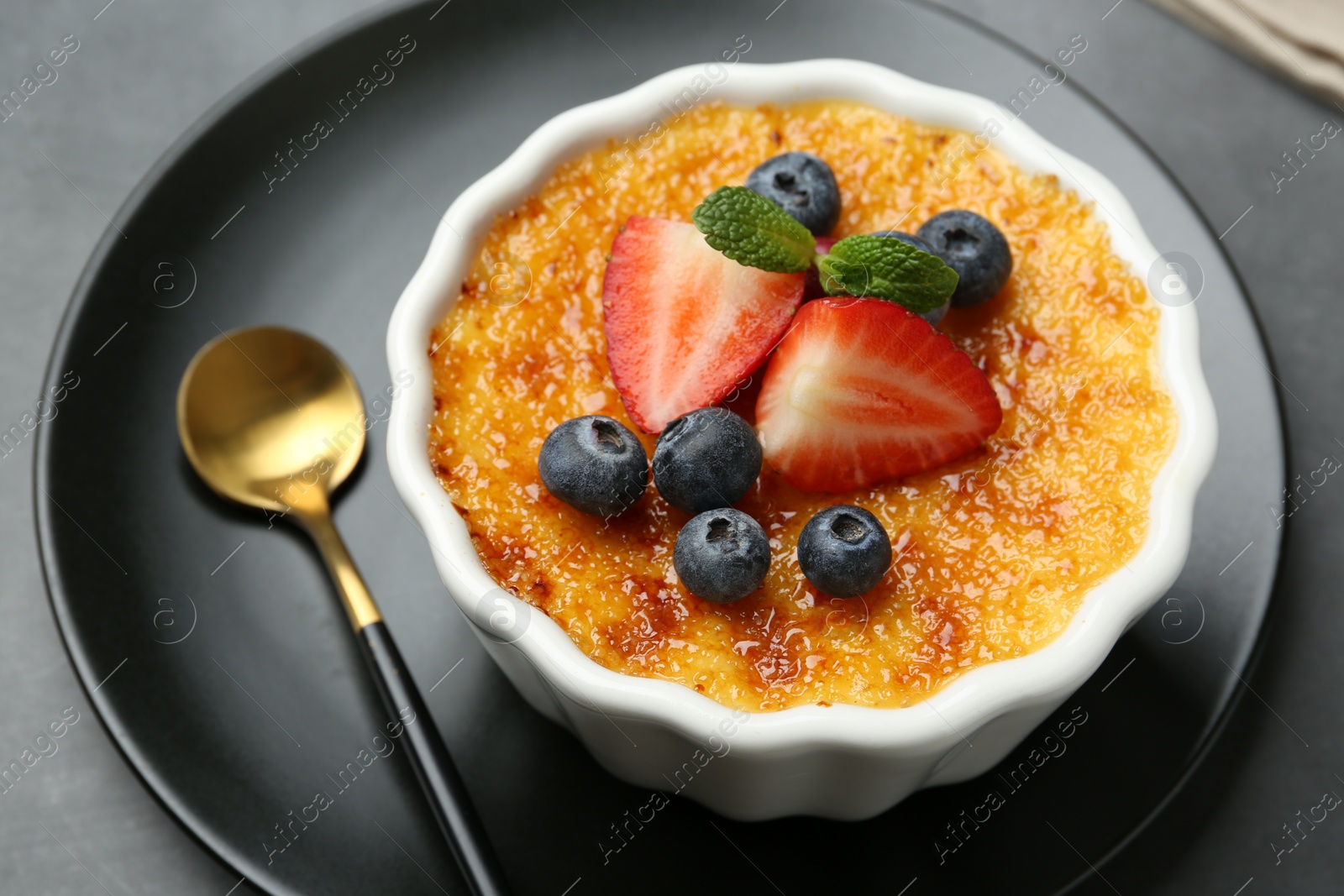 Photo of Delicious creme brulee with berries and mint in bowl on grey table, closeup