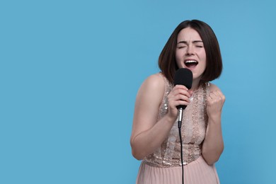 Beautiful young woman with microphone singing on light blue background, space for text