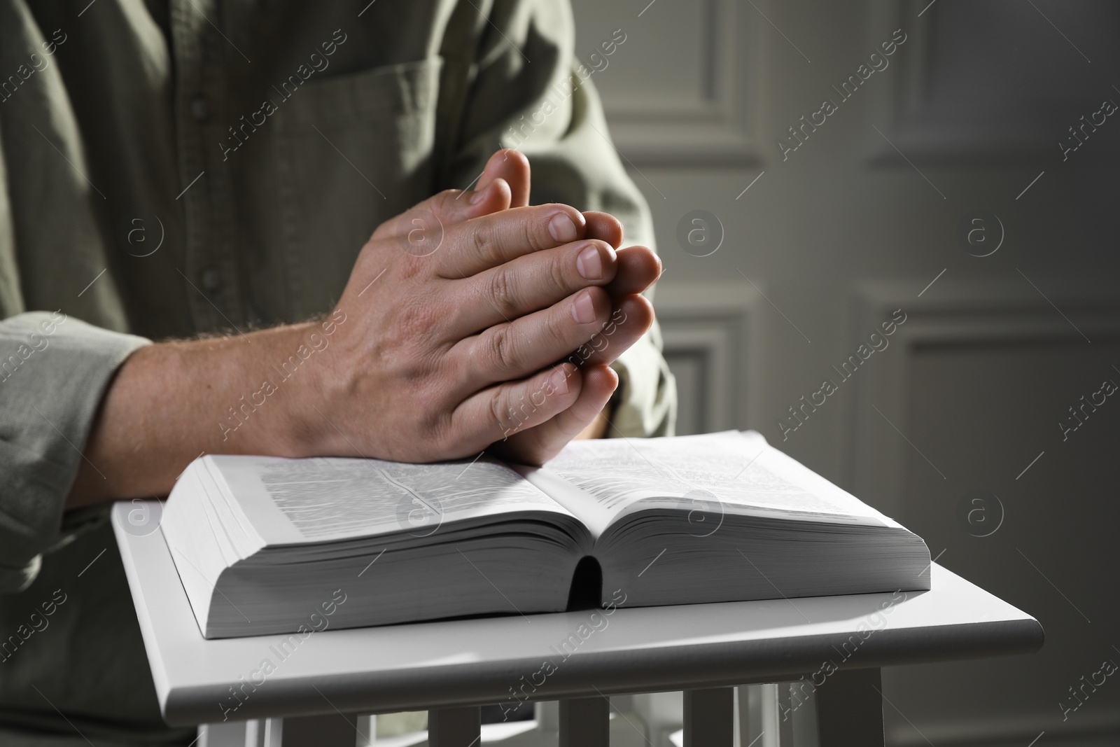 Photo of Religion. Christian man praying over Bible indoors, closeup