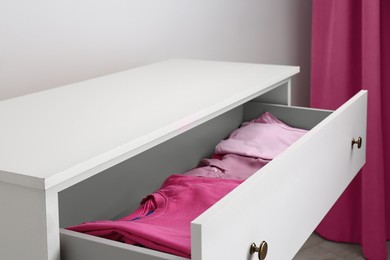 Photo of Many folded pink clothes in white chest of drawers indoors