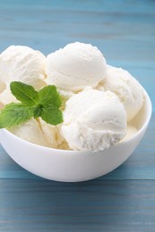 Photo of Delicious vanilla ice cream and mint in bowl on light blue wooden table, closeup