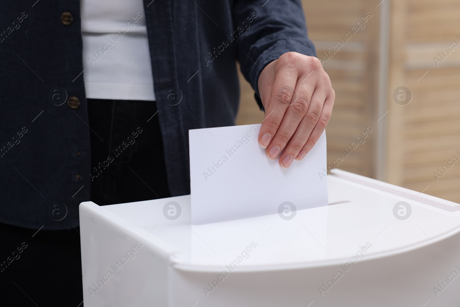 Photo of Woman putting her vote into ballot box on blurred background, closeup