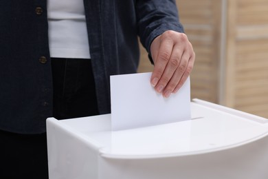 Photo of Woman putting her vote into ballot box on blurred background, closeup