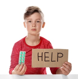 Photo of Little child with pills and word Help written on cardboard against white background. Danger of medicament intoxication