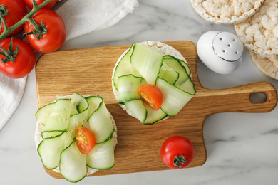Photo of Puffed rice cakes with vegetables served on white marble table, flat lay