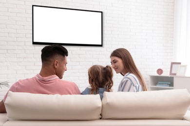 Photo of Family watching TV on sofa at home, back view