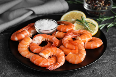 Photo of Delicious cooked shrimps with salt and lemon on dark grey table