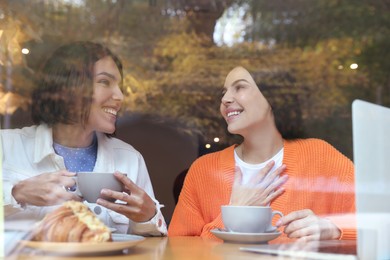 Photo of Special Promotion. Happy young women using laptop at table in cafe, view from outdoors