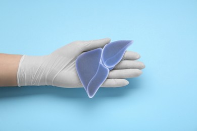 Photo of Doctor in glove holding paper liver on light blue background, closeup and top view. Hepatitis treatment