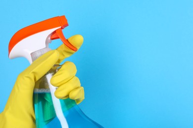 Woman holding plastic spray bottle on light blue background, closeup. Space for text