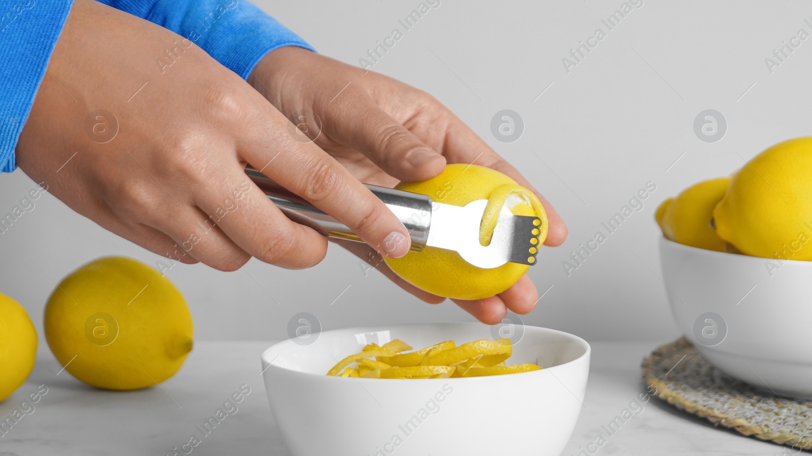 Photo of Woman zesting lemon at white marble table, closeup