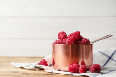 Saucepan with delicious ripe raspberries on wooden table against light background, space for text