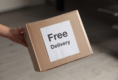 Photo of Courier holding parcel with sticker Free Delivery indoors, closeup