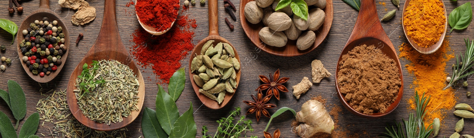 Image of Different herbs and spices with spoons on wooden table, flat lay. Banner design