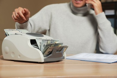 Photo of Man using banknote counter while talking on phone at wooden table indoors, closeup