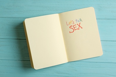 Photo of Notebook with phrase "LET'S TALK SEX" on light blue wooden background, top view, Space for text