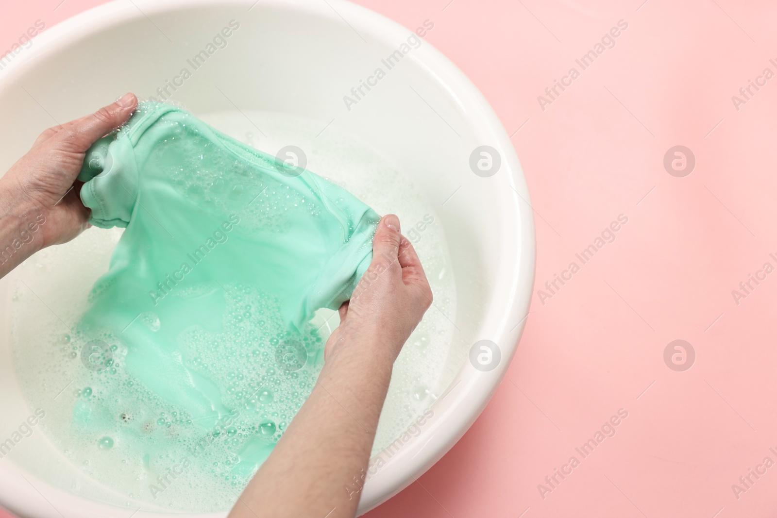 Photo of Woman washing baby clothes in basin on pink background, closeup