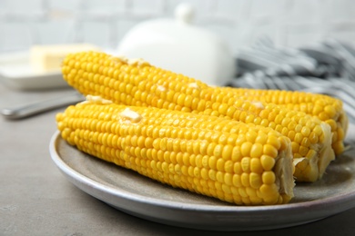 Photo of Plate of tasty boiled corn cobs with butter on light grey table, closeup