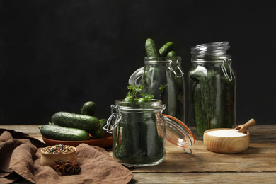 Photo of Pickling jars with fresh ripe cucumbers and spices on wooden table