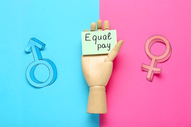 Photo of Gender pay gap. Wooden mannequin hand with paper note, male and female symbols on color background, flat lay