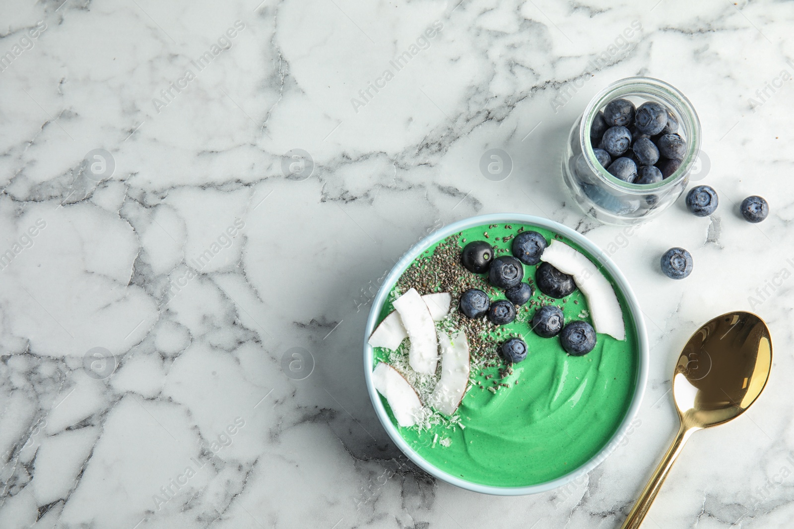 Photo of Bowl of spirulina smoothie and blueberries on marble background, top view with space for text