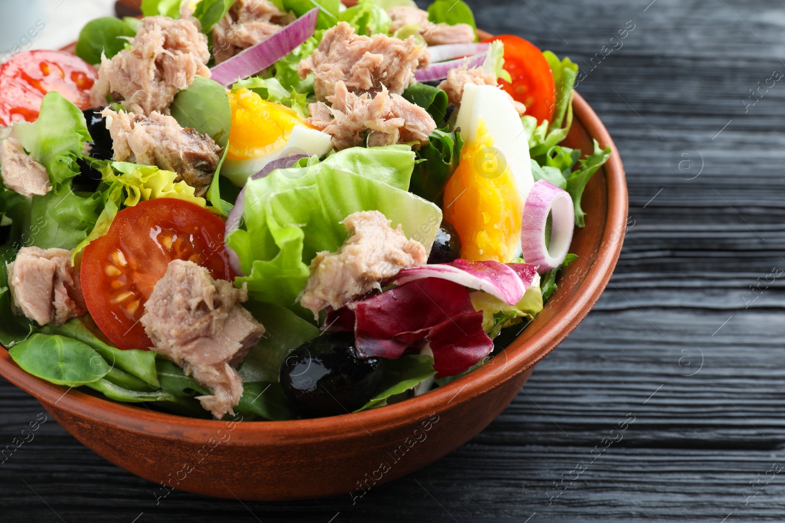 Photo of Bowl of delicious salad with canned tuna and vegetables on black wooden table, closeup