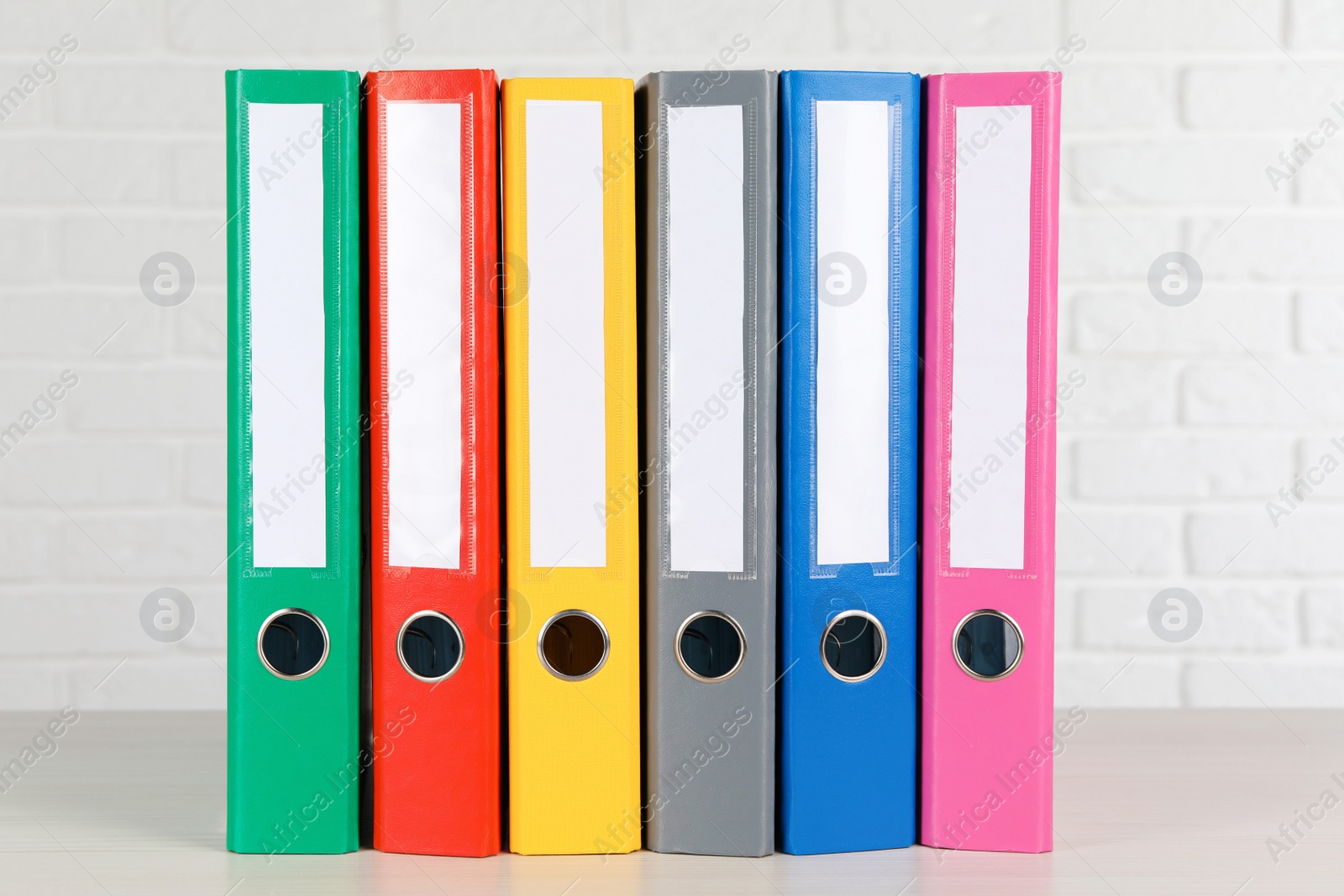 Photo of Many hardcover office folders on wooden table near white brick wall