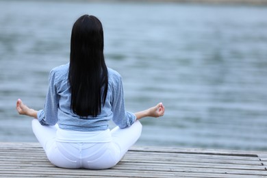 Photo of Young woman meditating near river, back view. Space for text