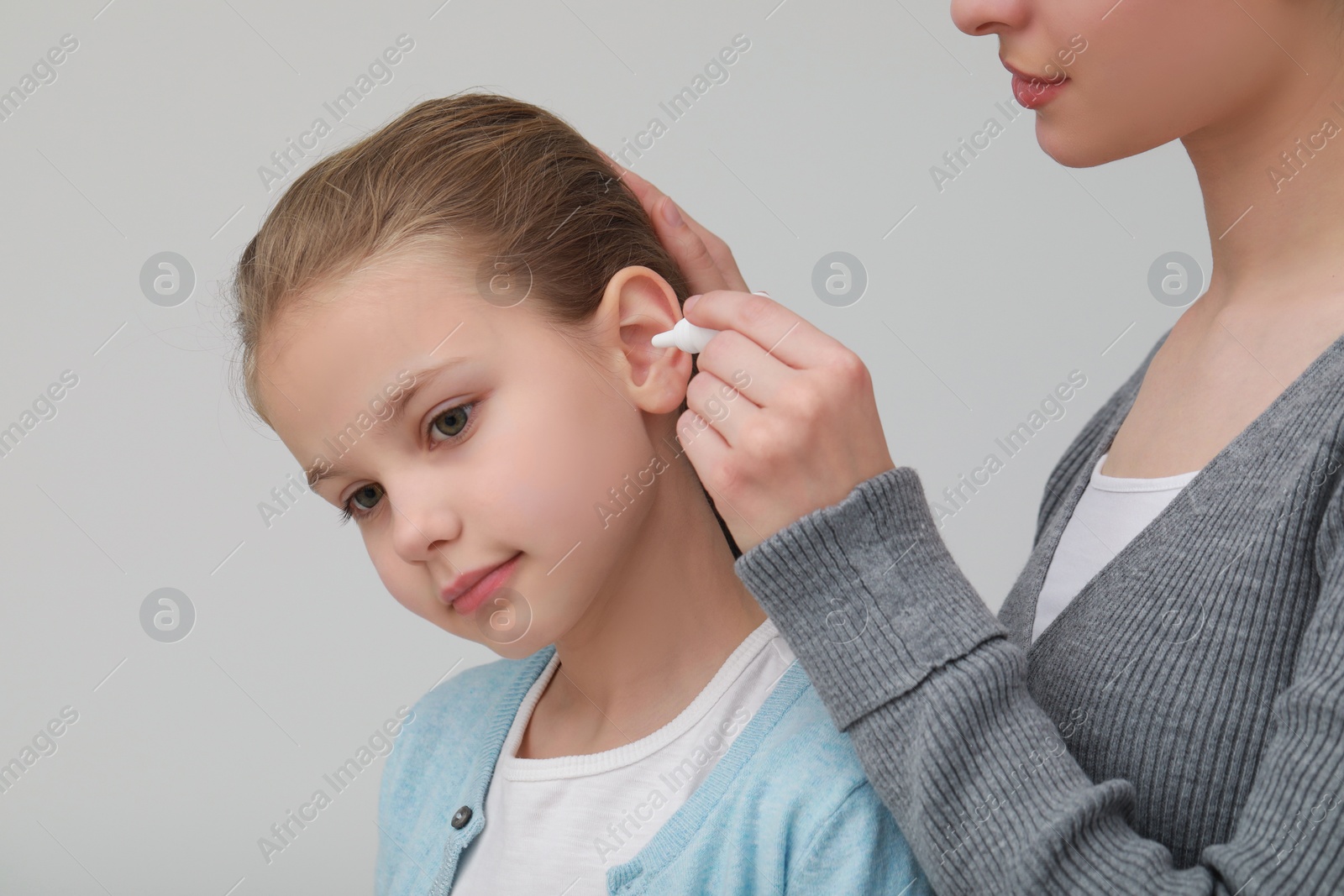 Photo of Mother dripping medication into daughter's ear on light grey background