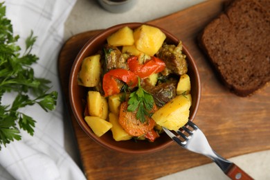 Photo of Tasty cooked dish with potatoes in earthenware served on light table, flat lay
