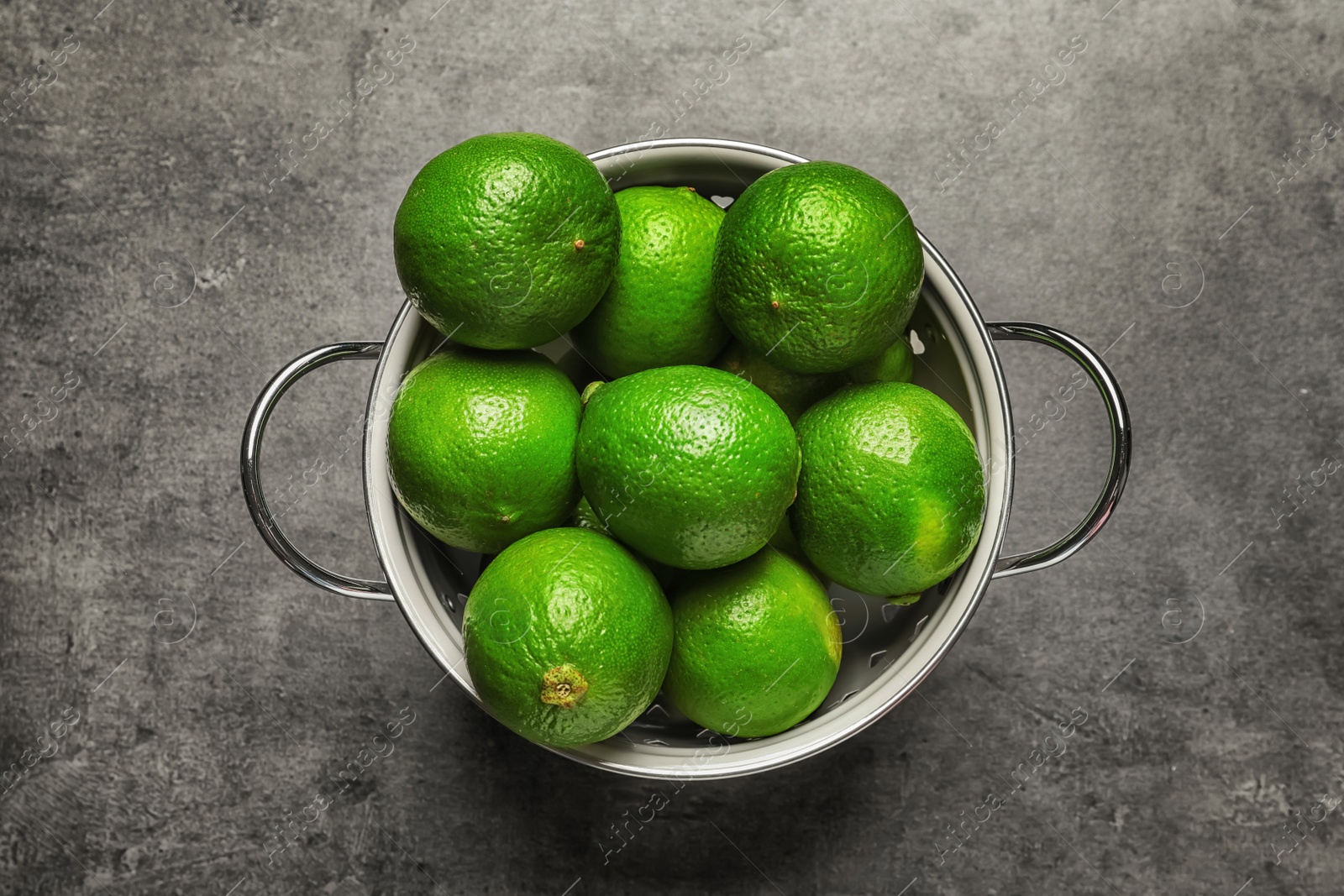 Photo of Colander with fresh ripe limes on gray background, top view