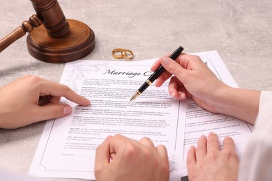 Man and woman signing marriage contract at light grey table, closeup