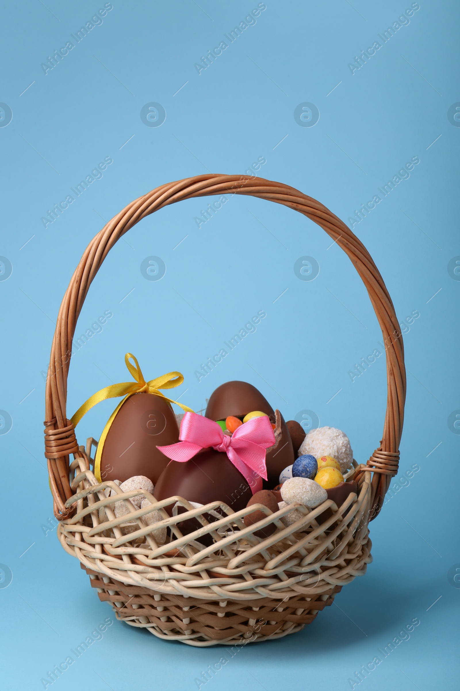 Photo of Wicker basket with tasty chocolate Easter eggs and different candies on light blue background