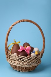 Wicker basket with tasty chocolate Easter eggs and different candies on light blue background