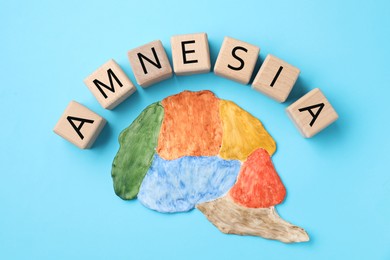 Photo of Word Amnesia made of wooden cubes and brain with sections on light blue background, flat lay