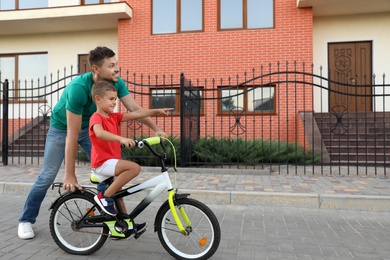 Photo of Happy father teaching his son to ride bicycle on street