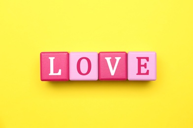 Cubes with word LOVE on yellow background, flat lay