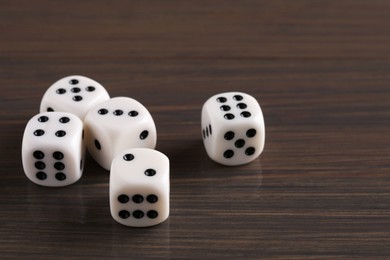 Photo of Many white game dices on wooden table, closeup. Space for text