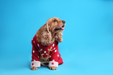 Adorable Cocker Spaniel in Christmas sweater on light blue background, space for text