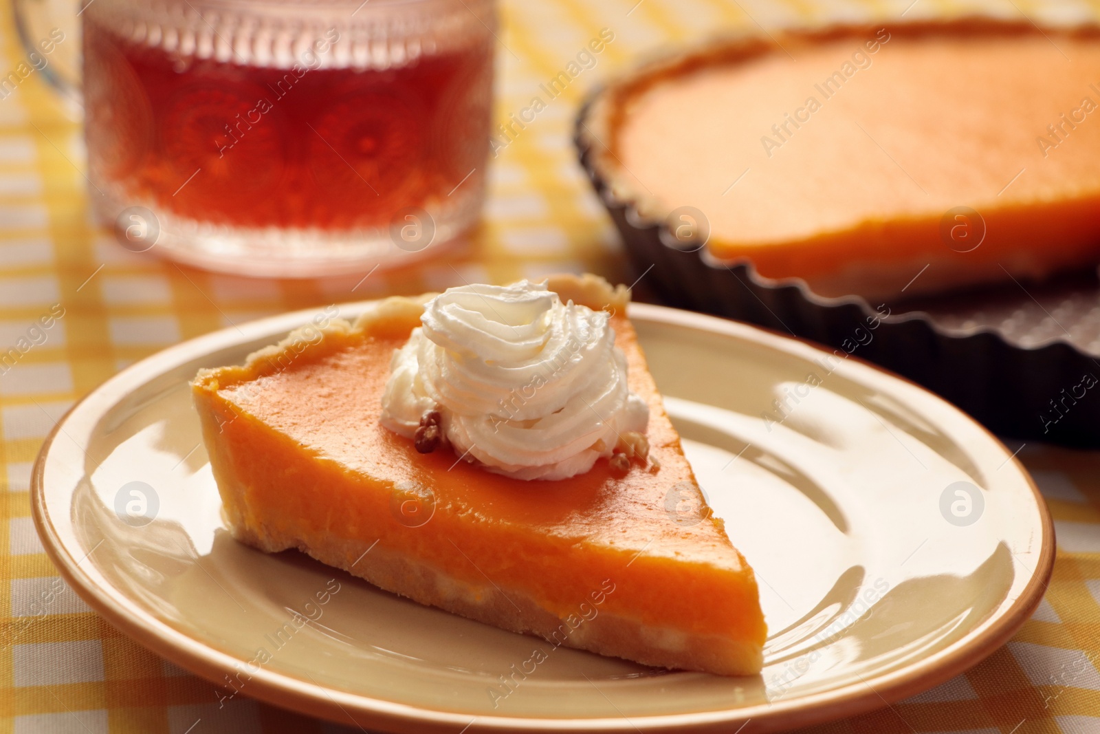 Photo of Piece of fresh homemade pumpkin pie served with whipped cream and tea on table, closeup