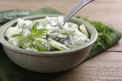 Photo of Eating delicious cucumber salad at wooden table, closeup