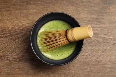 Photo of Cup of fresh green matcha tea with bamboo whisk on wooden table, top view