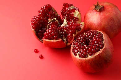 Photo of Whole and cut fresh pomegranates on red background, space for text