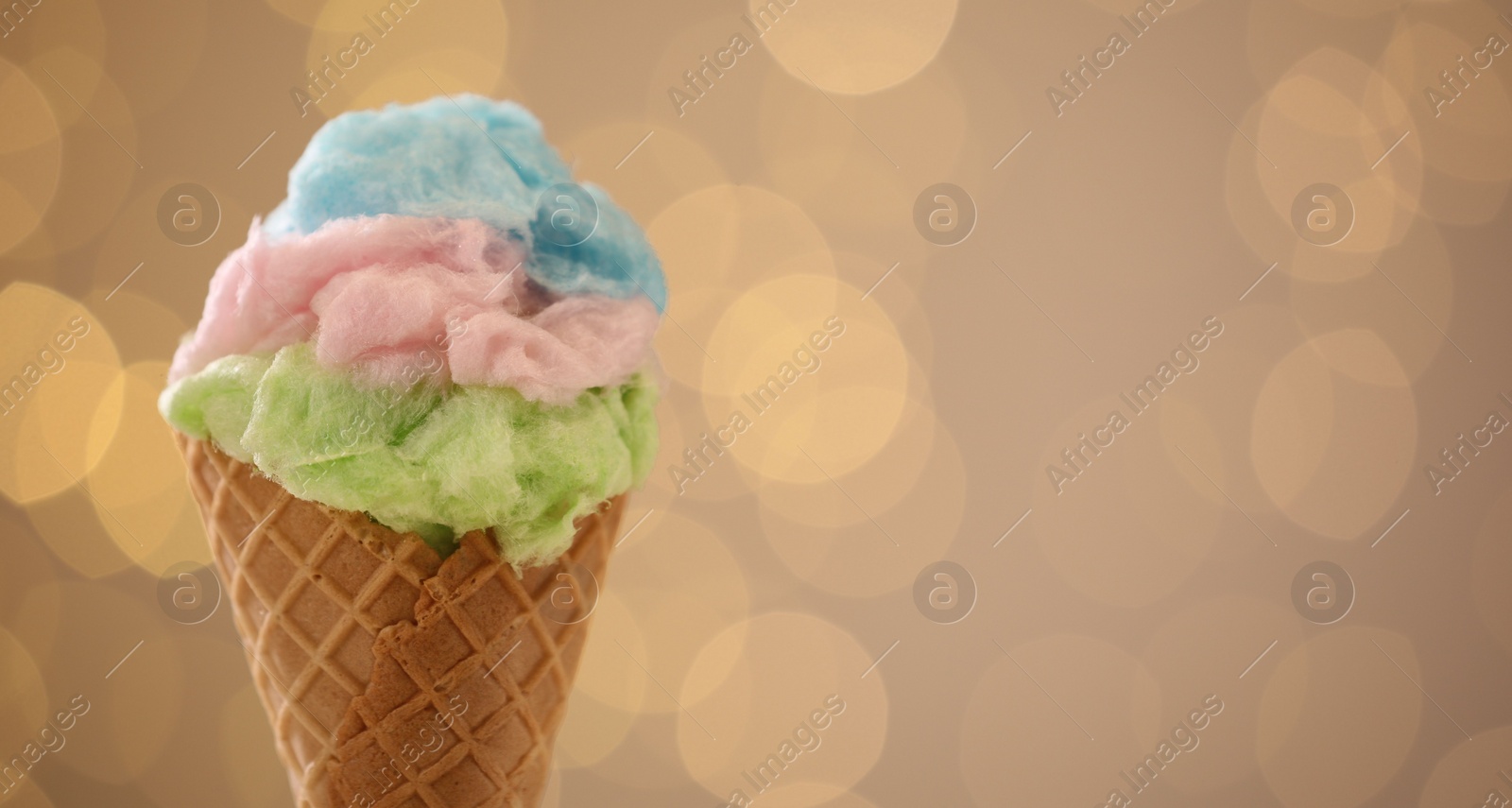 Photo of Sweet cotton candy in waffle cone against blurred lights, closeup. Space for text