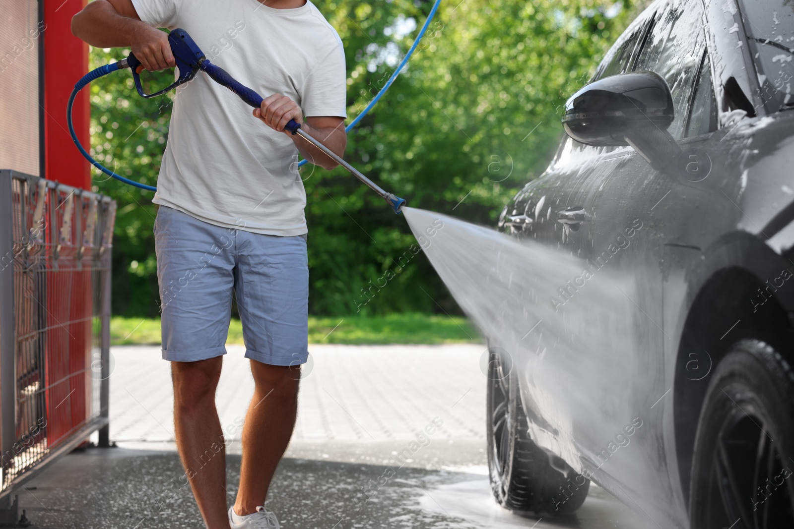 Photo of Man washing auto with high pressure water jet at outdoor car wash, closeup