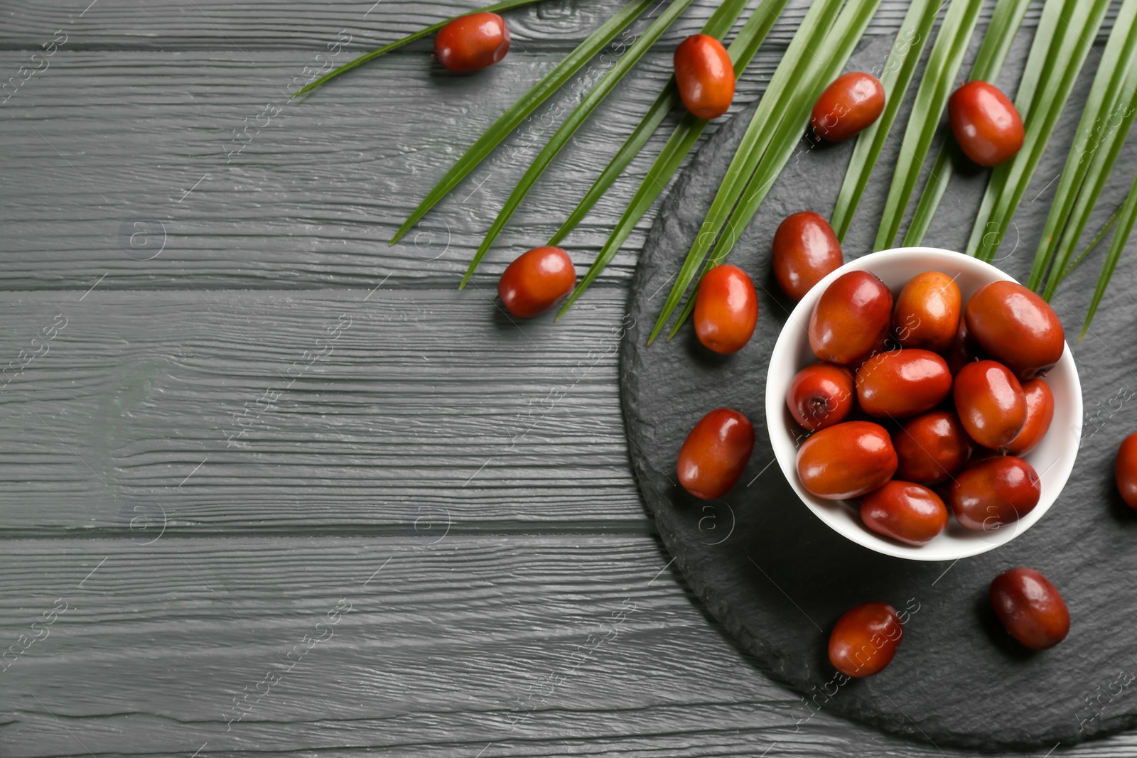 Photo of Palm oil fruits in bowl on grey wooden table, flat lay. Space for text