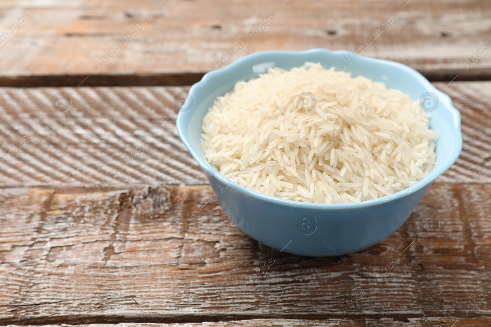 Photo of Raw basmati rice in bowl on wooden table, space for text