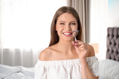 Young woman holding eyelash curler at home