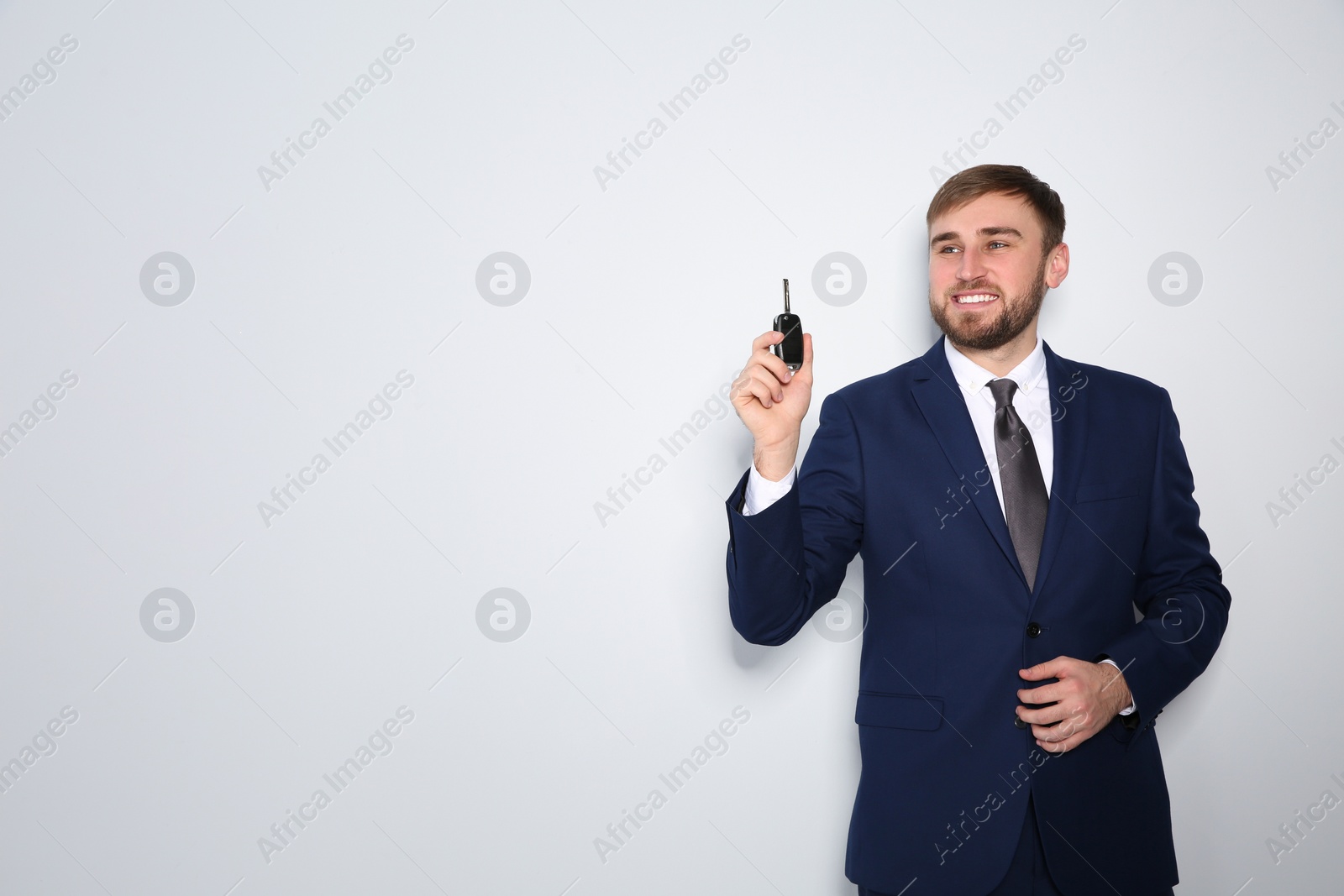 Photo of Happy young businessman with car key on grey background, space for text. Getting driving license